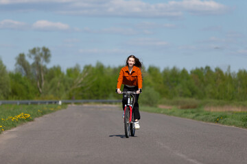 Young woman cycling on a rural road surrounded by greenery on a clear day in springtime