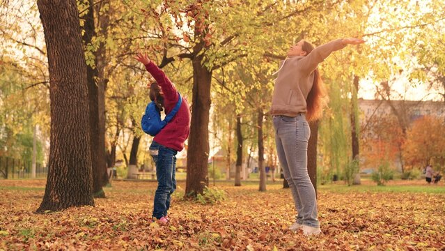 mother and little child in an autumn park throw dry leaves up, happy family, live fun with mom, cheerful kid plays with foliage and parent hands throwing leaf fall, parental care of girl, nature walk. - Powered by Adobe