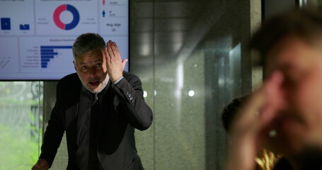 Angry manager shouting during tense business meeting in modern office with analytics presentation in background, scolding employee, workplace conflict and leadership stress