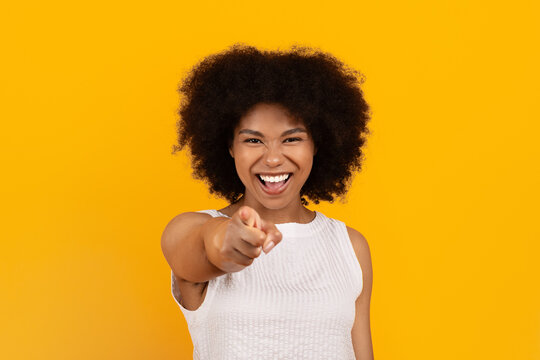 Smiling African American woman confidently pointing at camera on yellow studio background. Direct eye contact showing positivity, confidence, and empowerment