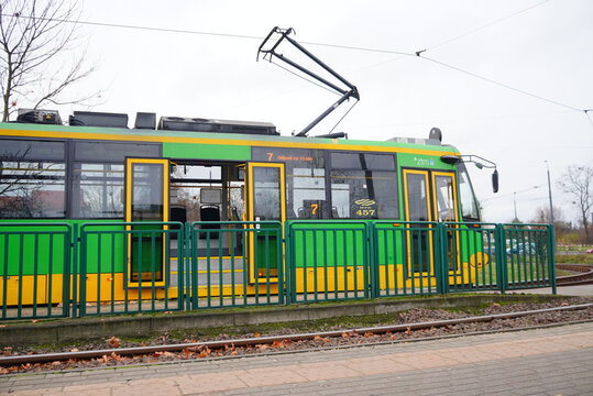 Green and yellow tram at a stop on a cloudy day