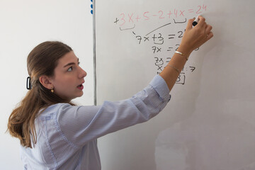 Young woman student solving a math equation on a whiteboard, explaining complex algebraic problems during a lesson, focusing on education, learning, and academic instruction