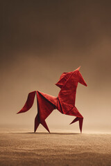 A beautiful red origami horse, artistic and unique, stands on a tan surface.