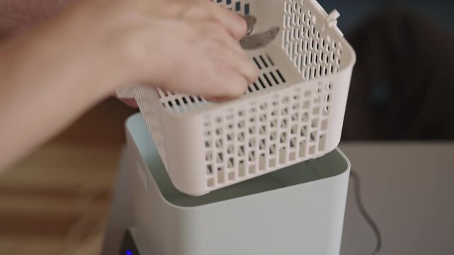Cleaning service employee loading modern ultrasonic cleaner at home with basket filled with forks and spoons for thorough and sterilizing wash using sonic technology, close-up. Shooting in slow motion