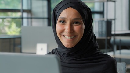 Happy positive muslim business woman in hijab smiling in office arabian ethnic islamic businesswoman female girl worker smile toothy looking at camera enjoying job in company professional manager