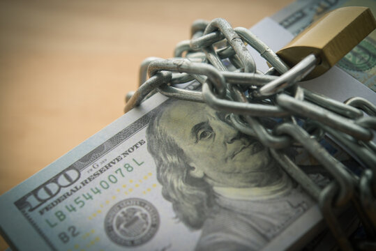 Close up heap US dollar banknotes in chain with padlock. Keeping or banning cash US dollars, money restrictions, frozen assets, dedollarisation, debt ceiling, business financial and so on concept.