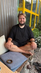 Portrait of a Smiling, Bearded Man Relaxing Cross-legged on a Bench Outdoors
