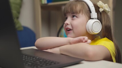 little schoolgirl headphones does homework while sitting digital laptop. distance learning online students. children funny communication through internet video communication. lessons monitor display - Powered by Adobe