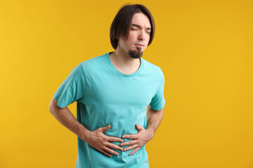 Obraz premium Man suffering from stomach ache and nausea on yellow background