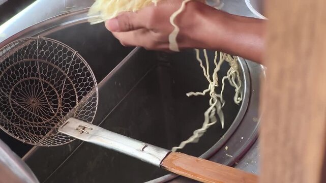 Vendor cooking Mie Ayam (Indonesian chicken noodles) in boiling water, preparing street food bowls.
