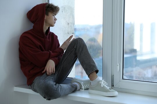 Depressed teenage boy near window at home, space for text - Powered by Adobe