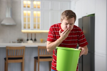 Young man with bucket suffering from nausea indoors, space for text © New Africa