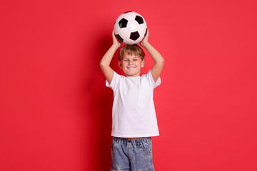 Cute boy with soccer ball on red background