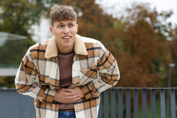 Young man suffering from stomachache and nausea outdoors. Space for text
