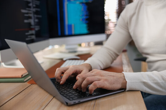 Programmer working on laptop at wooden table indoors, closeup