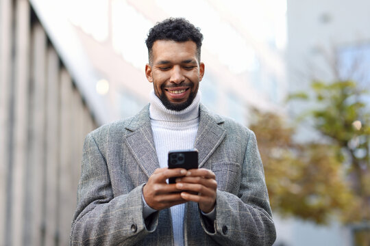 Smiling man in suit with smartphone on city street, low angle view