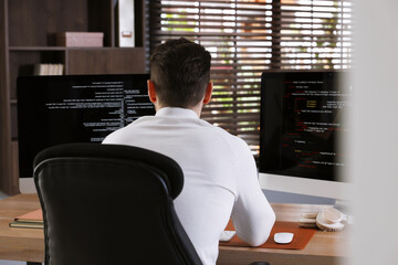 Programmer working on computer with dual monitors at table in office, back view