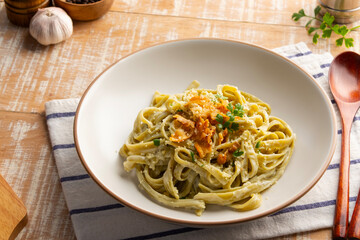Fettuccine spinach pasta with creamy carbonara sauce topped with crispy bacon and parmesan cheese in a plate.