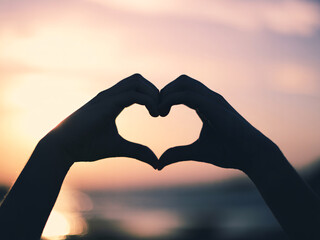 Warm sunset silhouettes loving hands forming a heart shape, symbolizing romance, connection, and passion during golden hour.