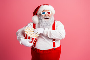 Santa with popcorn and three dimensional glasses in a pink studio enjoying a festive moment