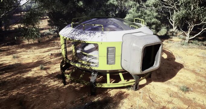 A round, green pod sits on a sunlit patch of earth surrounded by dense trees and vegetation. The unique structure blends technology with nature in a peaceful setting.