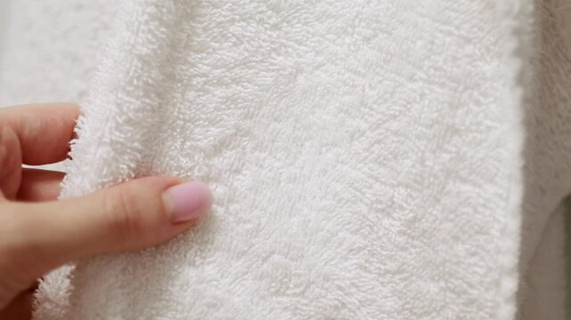 Hand touching soft white bath towel surface. Concept of fabric softness, laundry care, fabric softener and bleach for clean and fresh linens