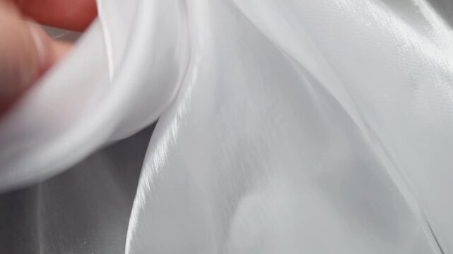 Female hand gently checking glossy satin material creating soft flowing white fabric folds