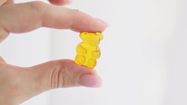 Close-up of fingers holding a soft gummy bear candy made of gelatin. Concept of CBD gummies, vitamin supplements for kids, healthy treats, and nutritional candy. Colorful chewy texture symbolizing fun
