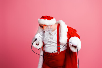 Santa in red suit sings into microphone with fluffy beard against pink background for festive holiday mood