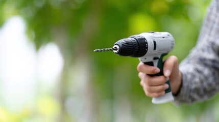 Naklejka premium Cordless drill held by person with blurred green background, showing focus on drill bit ready for use in outdoor setting