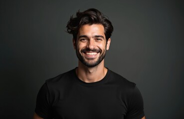 Fototapeta premium Young man with beard and styled hair smiles in a black t-shirt. His friendly expression and dark background make him ideal for professional or lifestyle content. He looks confident and approachable.