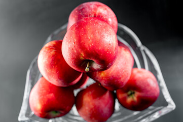 A still life composition featuring red ripe apples arranged in a clear glass vase against a black background.