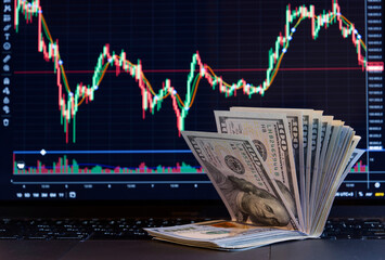 Stack of hundred-dollar bills against a crypto exchange chart.