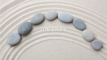 Five smooth grey pebbles arranged in an arc on raked sand with the word journey