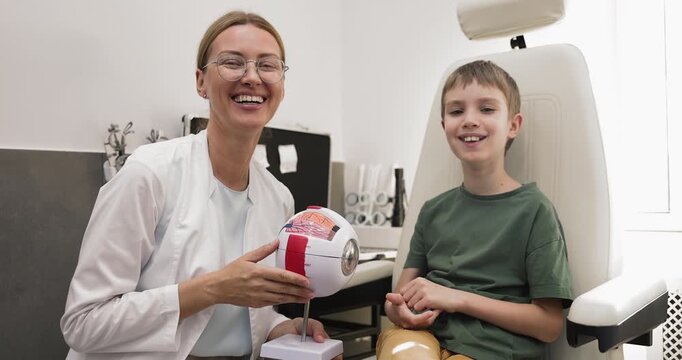 Optometrist holding eye model posing for camera with little patient