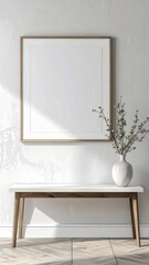 Blank picture frame on a white wall above a wooden bench with a vase of branches minimalist home decor.