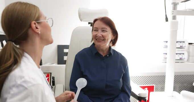 Optometrist holds occluder, talks with elderly patient during eye checkup