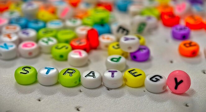 Colorful beads spell out STRATEGY surrounded by a blurred array of other letter beads. A vibrant visual representing planning and thought process.