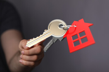 Person's hand holds house keys with a red house keychain symbolizing home ownership. Concept of real estate, mortgage, and buying a house. Perfe