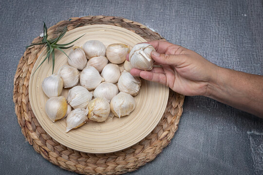 Hand holding solo garlic bulb from bamboo bowl