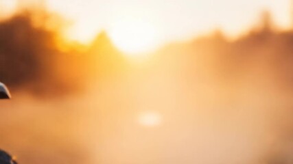An ATV driver rides toward the viewer, bathed in a warm, golden sunset