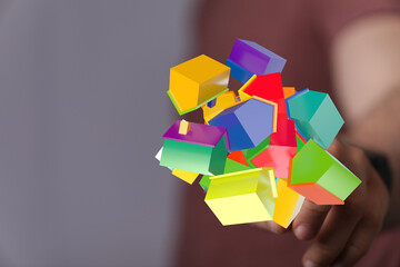 Close-up of hand holding abstract 3D house models in various colors. Concepts of real estate,...