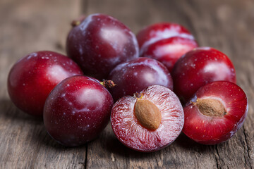 Close-up of fresh red and purple plums, some halved showing pits, on rustic wood.