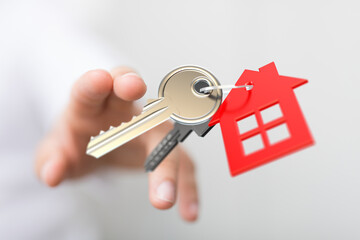 A hand holding keys with a red house-shaped keychain, symbolizing home ownership, real estate, and the dream of owning a house. Perfect for prop