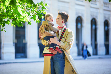 Beautiful young mother and her adorable toddler daughter walking together in park in Paris, France.