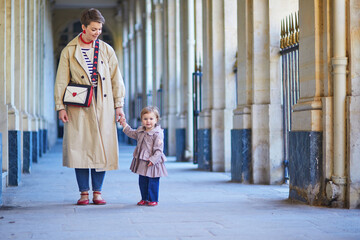 Beautiful young mother and her adorable toddler daughter walking together in park in Paris, France.