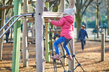 Fototapeta premium A young girl in warm winter clothing balancing and climbing on wooden playground equipment outdoors