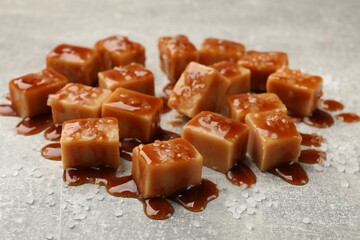 Tasty candies with salt and caramel sauce on grey textured table, closeup