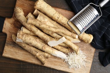Grated horseradish, grater and fresh roots on wooden table, top view