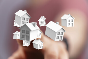 A hand holding a collection of floating houses, representing real estate, property investment and...